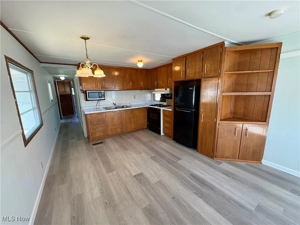 Kitchen with light countertops, brown cabinetry, light wood-type flooring, freestanding refrigerator, and pendant lighting