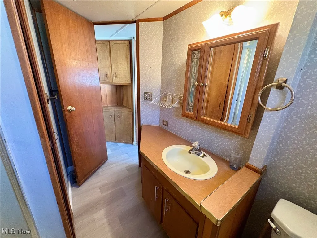 Half bath featuring vanity, wallpapered walls, and crown molding