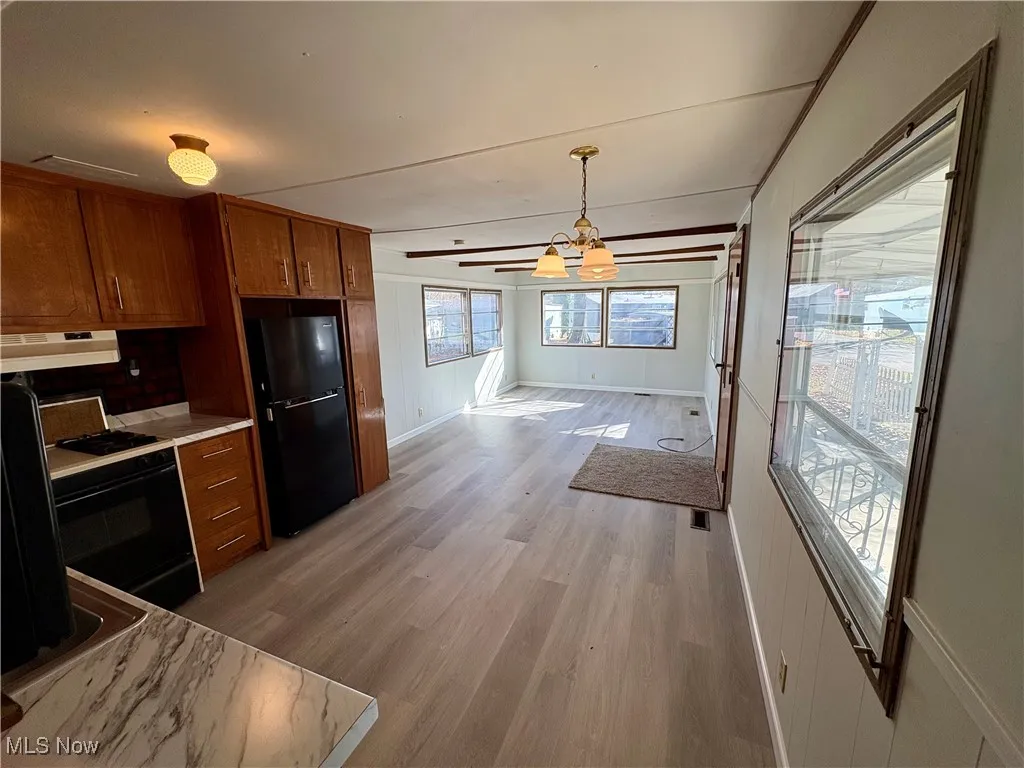Kitchen featuring light wood-style floors, light countertops, brown cabinetry, and black appliances