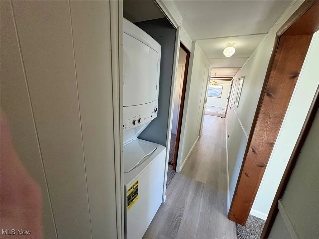 Laundry room featuring light wood-style flooring and stacked washing machine and dryer