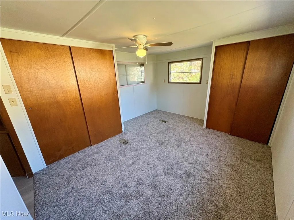 Unfurnished bedroom featuring carpet, a ceiling fan, and two closets