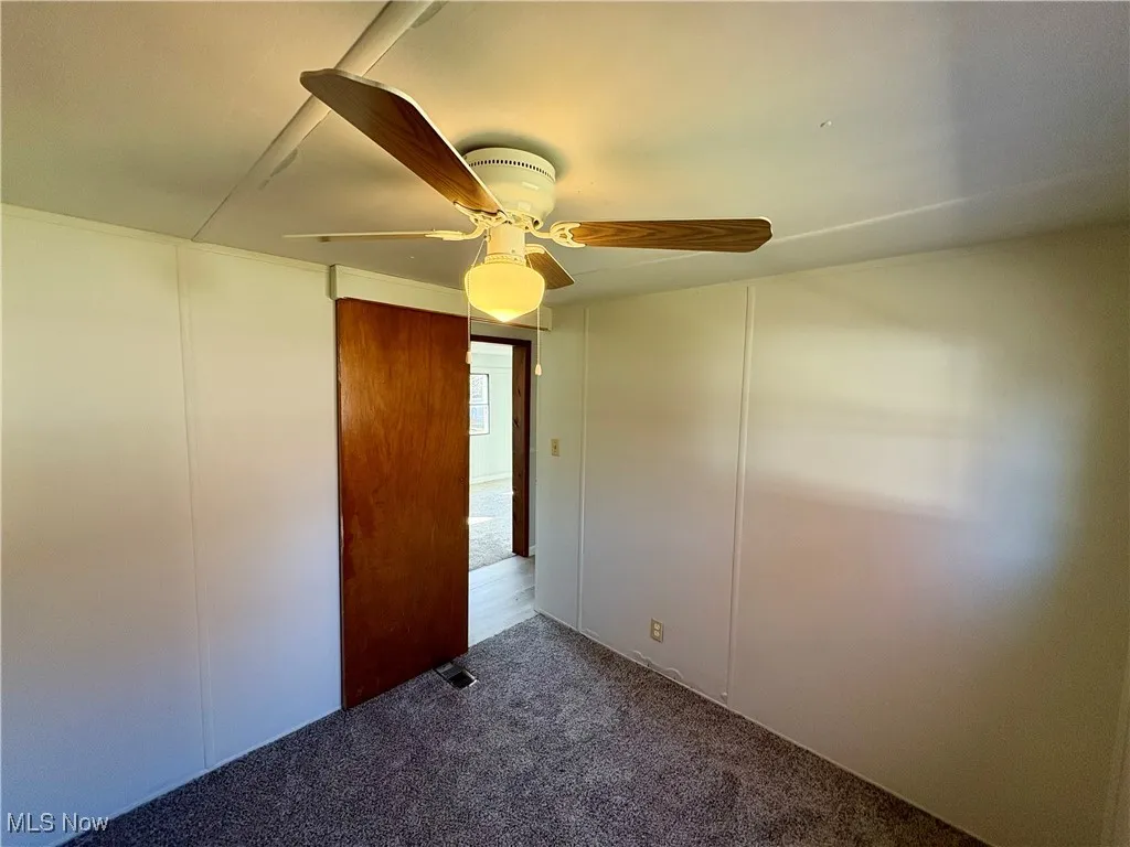 Empty room with a decorative wall, carpet floors, and ceiling fan