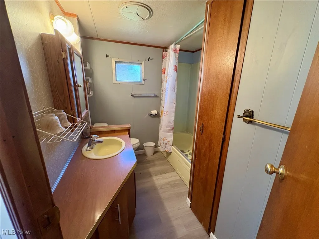Full bath featuring wood finished floors, curtained shower, vanity, and ornamental molding