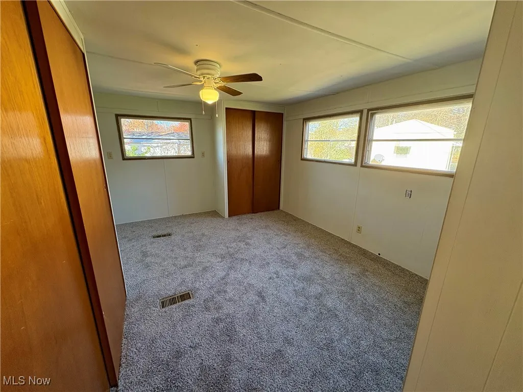 Unfurnished bedroom with carpet floors, a closet, multiple windows, and a ceiling fan