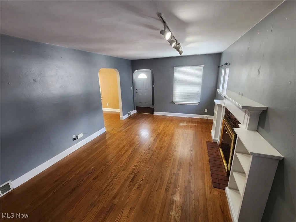 Unfurnished living room with arched walkways, track lighting, a brick fireplace, and dark wood finished floors