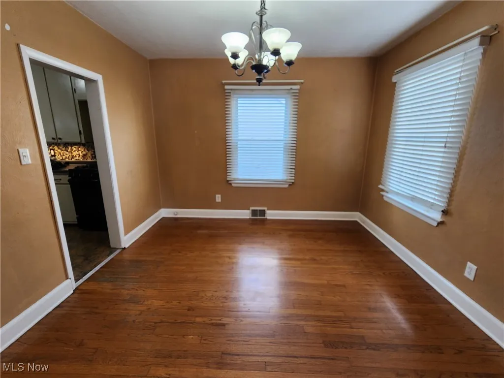 Unfurnished dining area featuring dark wood-style flooring, a chandelier, and healthy amount of natural light