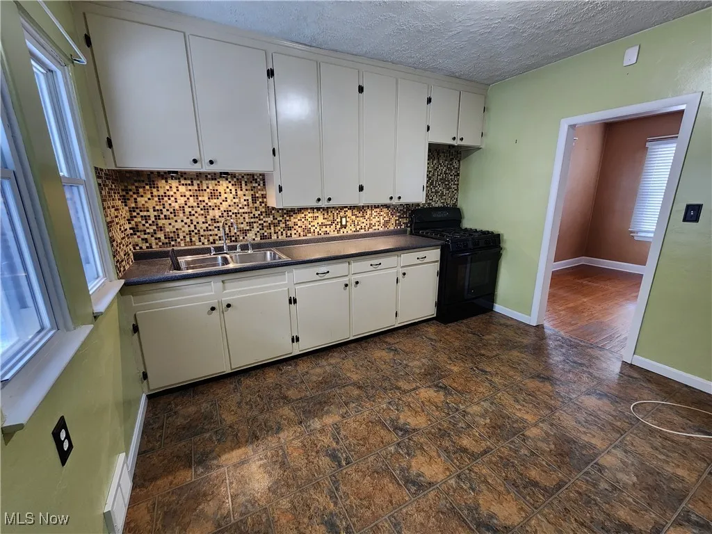 Kitchen with dark countertops, tasteful backsplash, gas stove, white cabinetry, and a textured ceiling