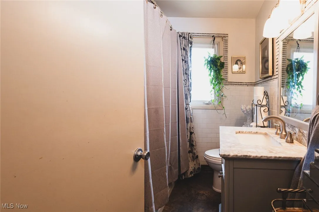 Full bathroom featuring vanity, tile walls, a shower with shower curtain, and a wainscoted wall