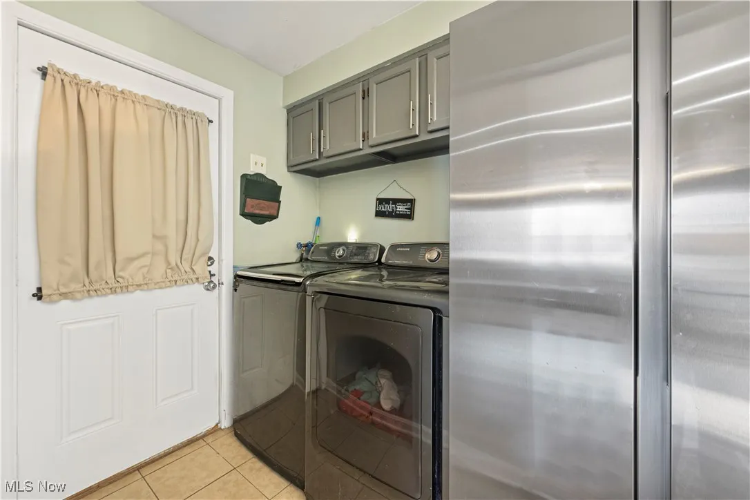Washroom with light tile patterned flooring and washing machine and clothes dryer