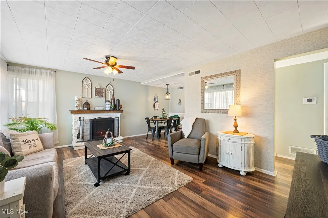 Living room with dark wood-style floors, a ceiling fan, and a fireplace
