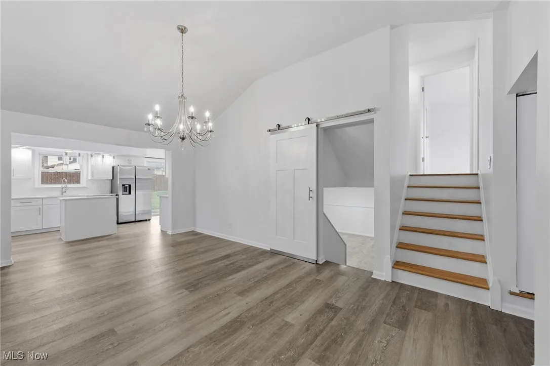 Unfurnished living room featuring a barn door, a chandelier, stairs, lofted ceiling, and light wood-style flooring