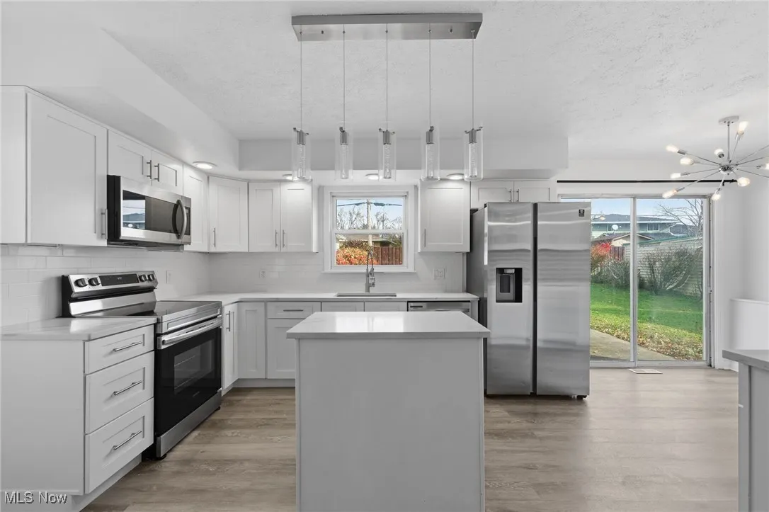 Kitchen with appliances with stainless steel finishes, a center island, hanging light fixtures, decorative backsplash, and light wood-style flooring