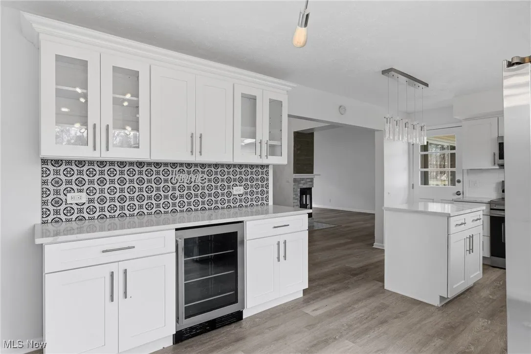 Kitchen featuring decorative backsplash, white cabinetry, beverage cooler, and light stone counters