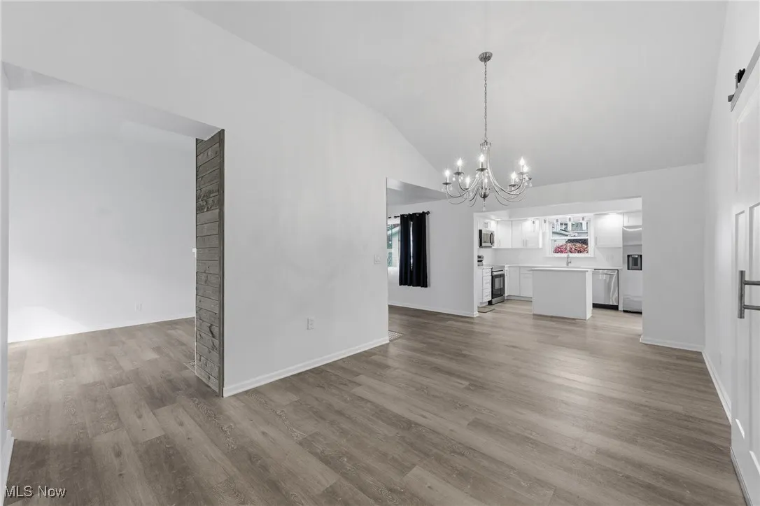 Unfurnished living room with light wood finished floors, vaulted ceiling, a barn door, and a chandelier