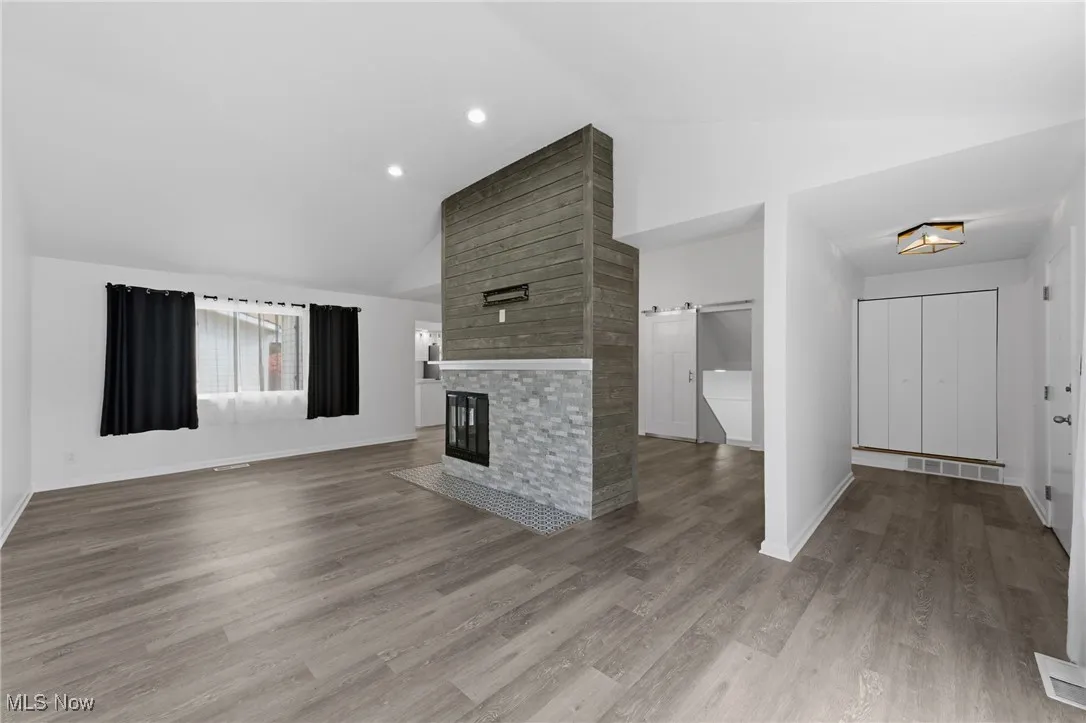 Unfurnished living room with light wood-style flooring, a large fireplace, a barn door, high vaulted ceiling, and recessed lighting