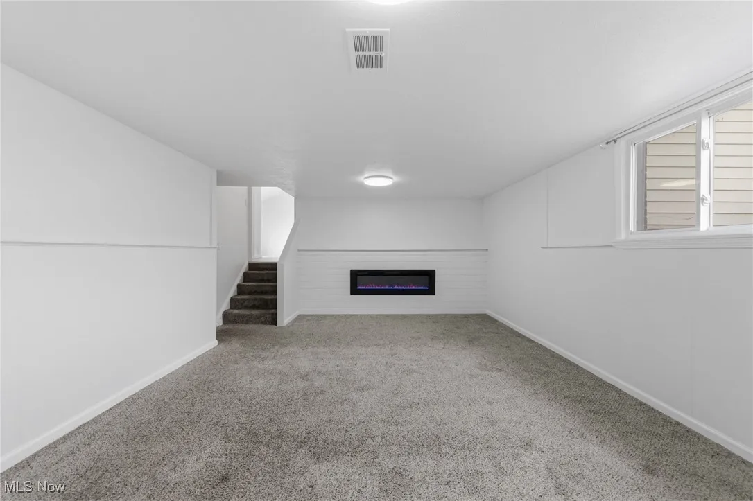 Unfurnished living room with light carpet, a glass covered fireplace, and stairs