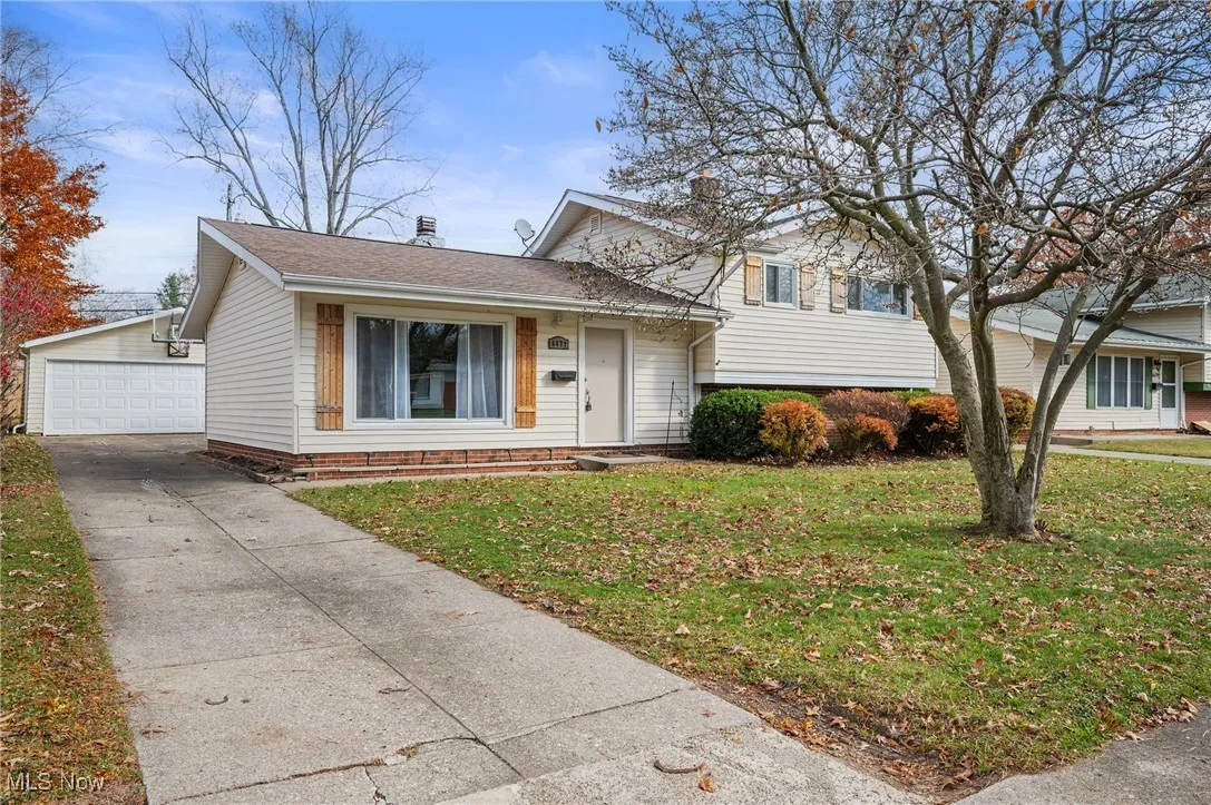 Tri-level home with a front yard, an outbuilding, a shingled roof, and a garage