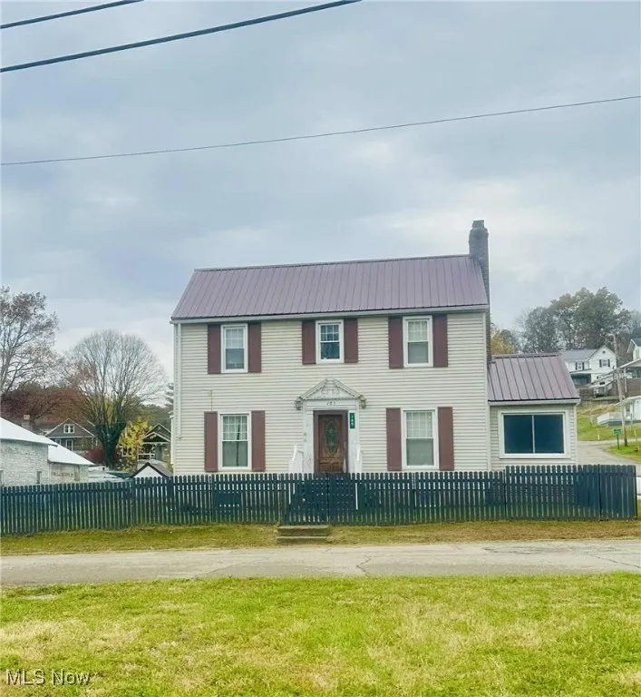 View of front facade with a metal roof, a fenced front yard, and a chimney