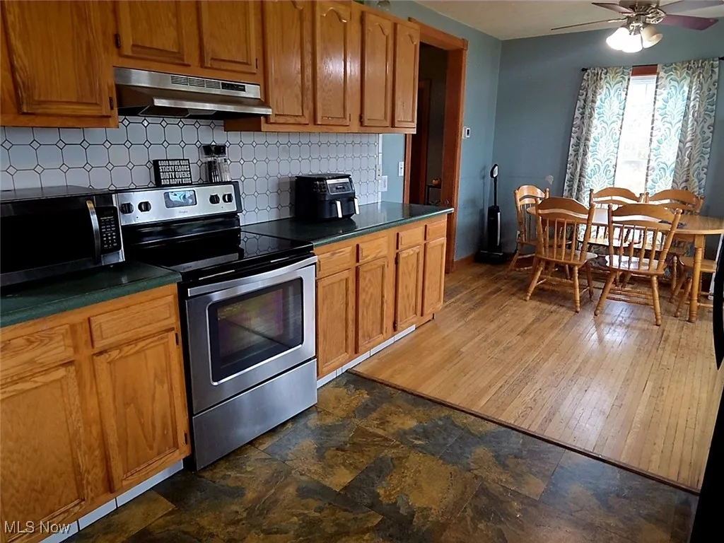 Kitchen with appliances with stainless steel finishes, decorative backsplash, dark countertops, under cabinet range hood, and brown cabinets