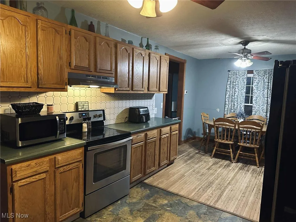 Kitchen with appliances with stainless steel finishes, dark countertops, backsplash, under cabinet range hood, and a textured ceiling
