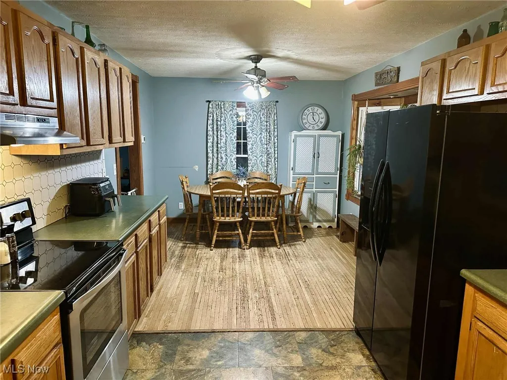 Kitchen with stainless steel range with electric stovetop, black refrigerator with ice dispenser, tasteful backsplash, under cabinet range hood, and a textured ceiling