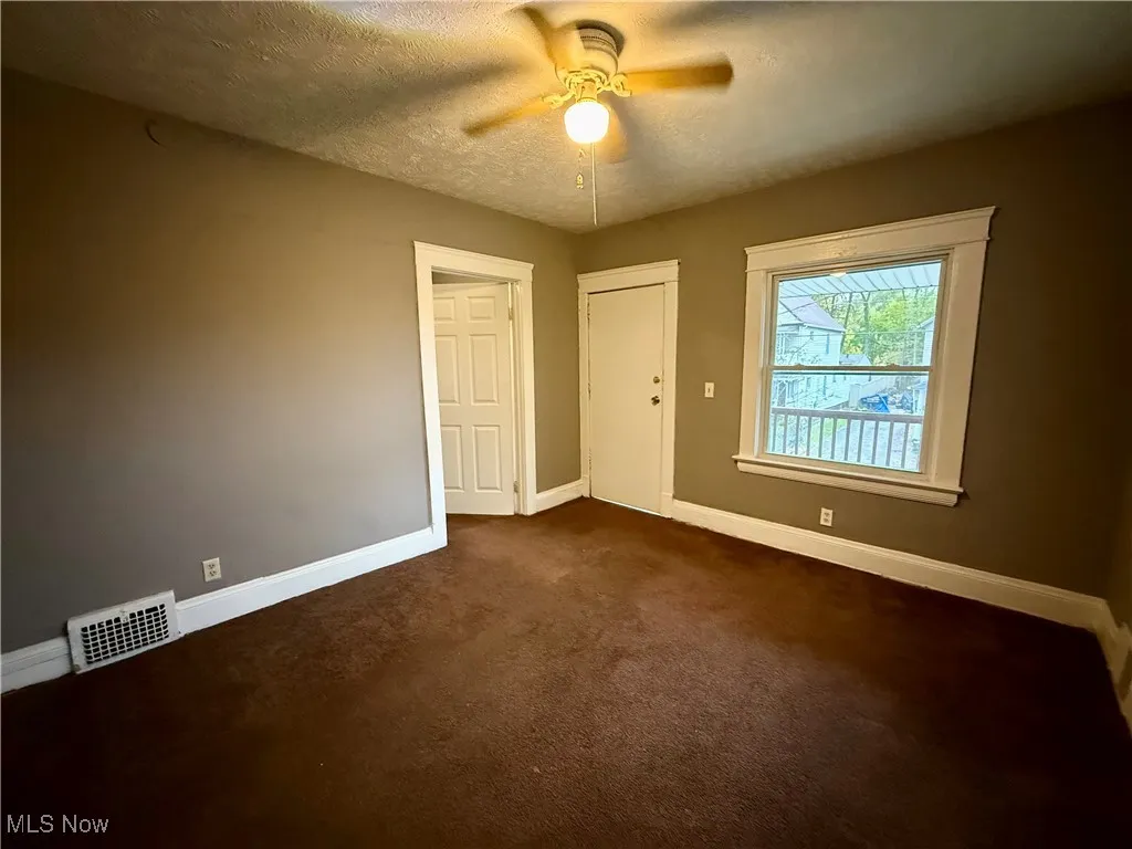 Spare room featuring a textured ceiling, dark carpet, and a ceiling fan