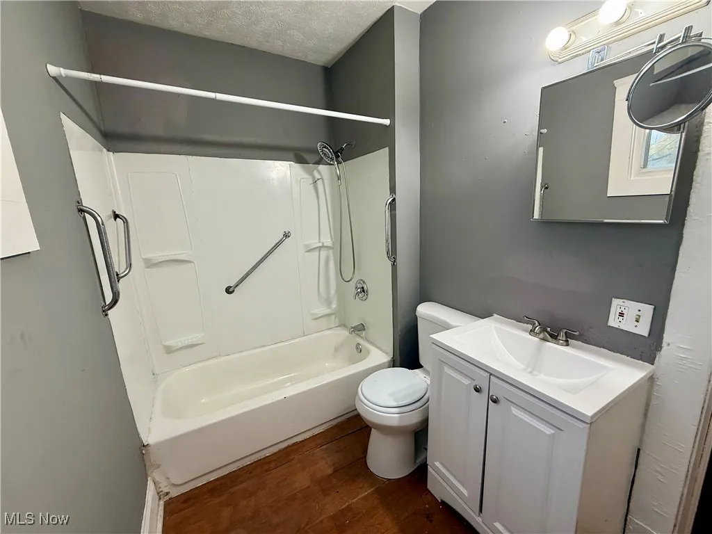 Bathroom with vanity,  shower combination, dark wood-type flooring, and a textured ceiling