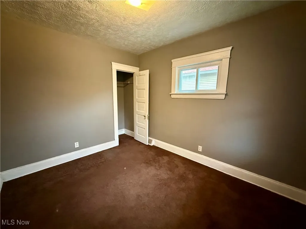 Unfurnished bedroom featuring a textured ceiling, dark carpet, and a closet