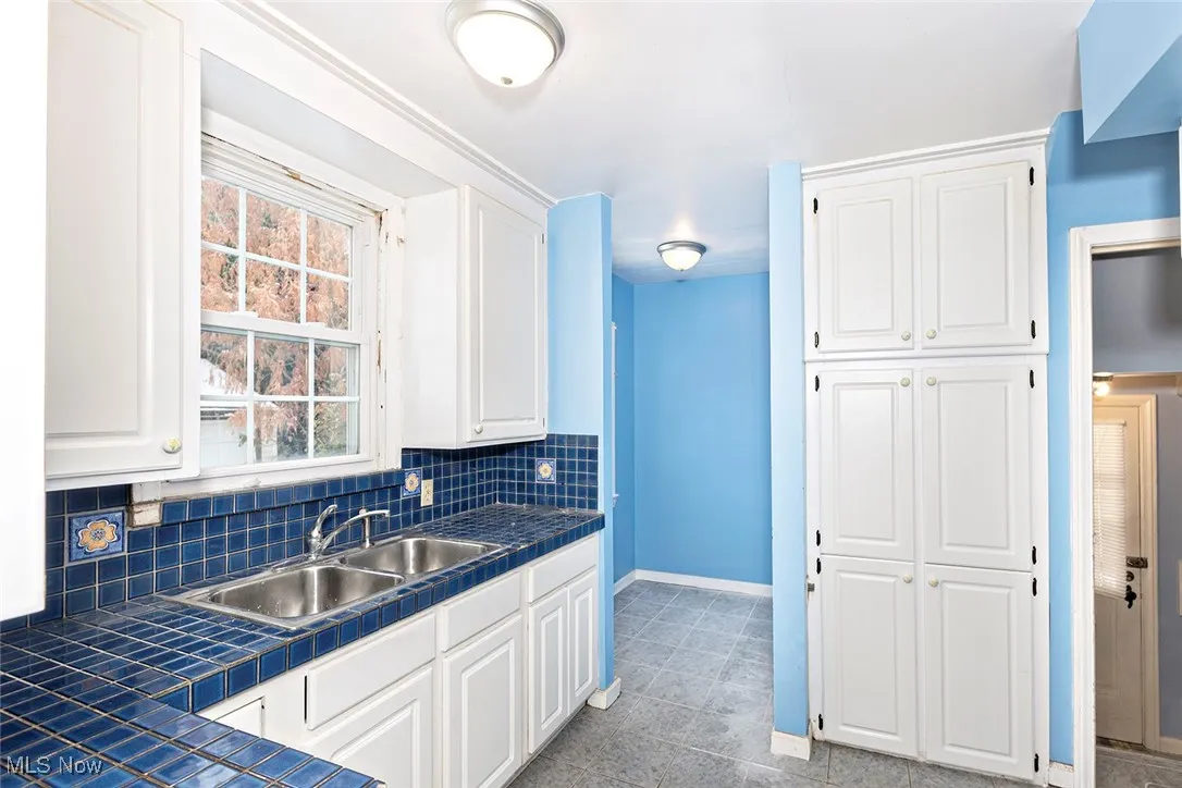 Kitchen with tile counters, white cabinets, and tasteful backsplash