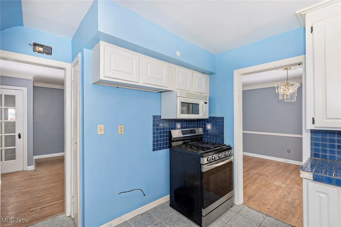 Kitchen featuring backsplash, stainless steel gas range, and white cabinets