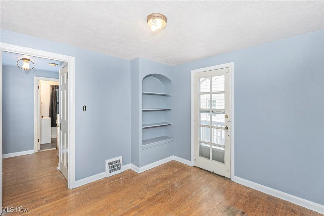 Unfurnished room with built in shelves, light wood-type flooring, and a textured ceiling