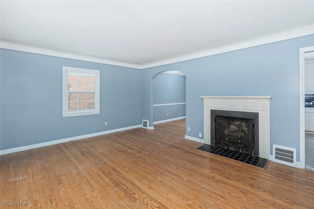 Unfurnished living room with arched walkways, a tile fireplace, and wood finished floors