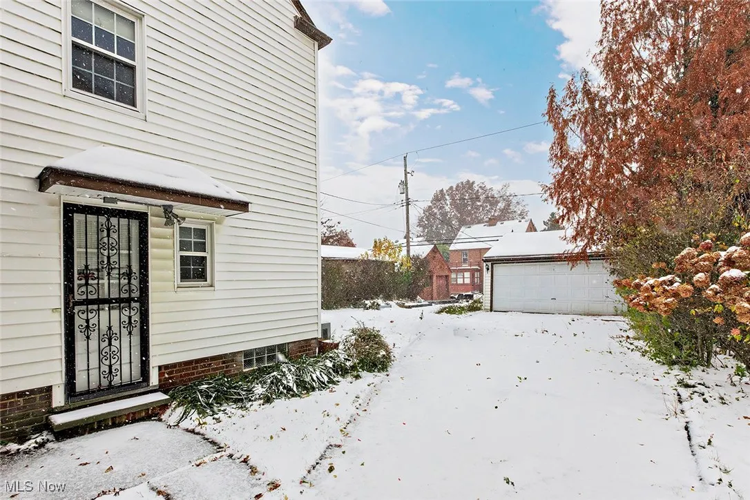 View of snowy exterior with an outdoor structure and a detached garage