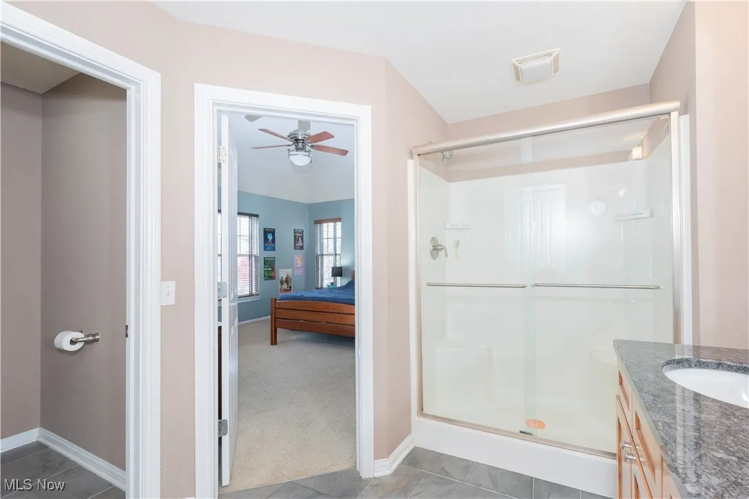 Ensuite bathroom featuring vanity, light colored carpet, a shower stall, a ceiling fan, and light tile patterned flooring