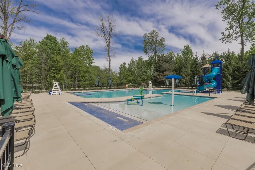Community pool featuring a patio, view of scattered trees, and a water play area