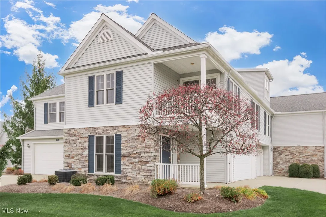 View of front facade featuring a garage, a balcony, stone siding, concrete driveway, and a front yard