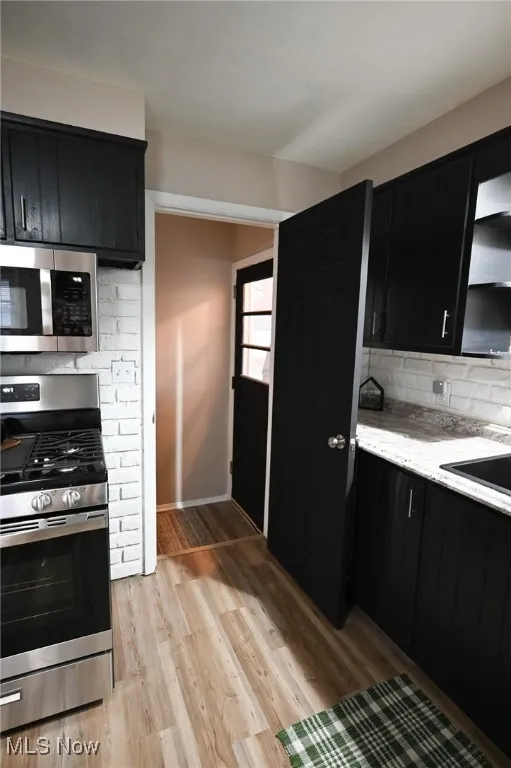 Kitchen featuring dark cabinets, stainless steel appliances, light stone counters, and backsplash