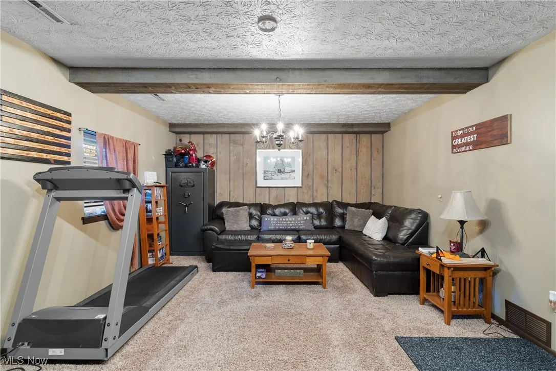 Living room with carpet, a chandelier, beamed ceiling, wooden walls, and a textured ceiling
