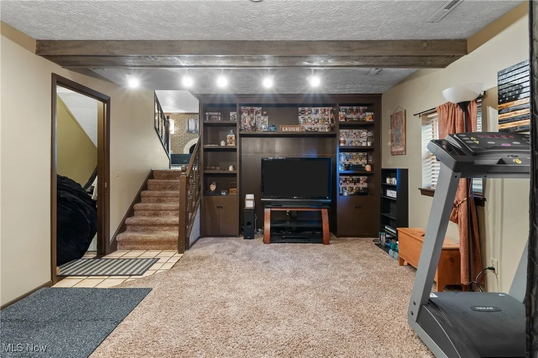 Living area featuring light colored carpet, a textured ceiling, beam ceiling, and stairway