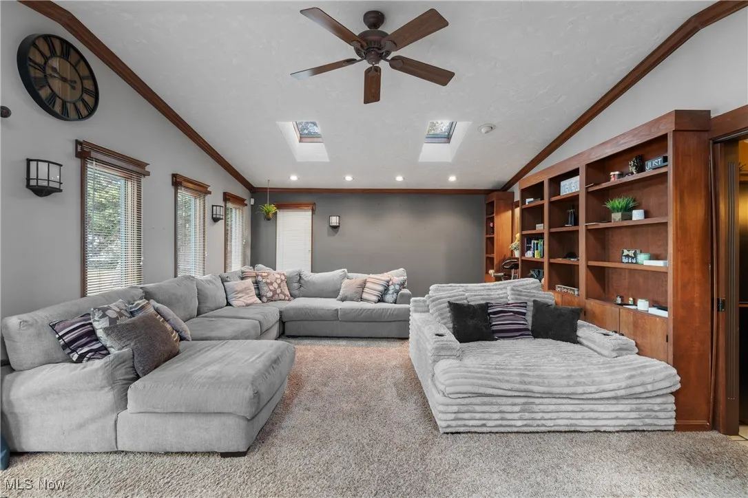 Living room featuring carpet floors, crown molding, a skylight, a ceiling fan, and a textured ceiling