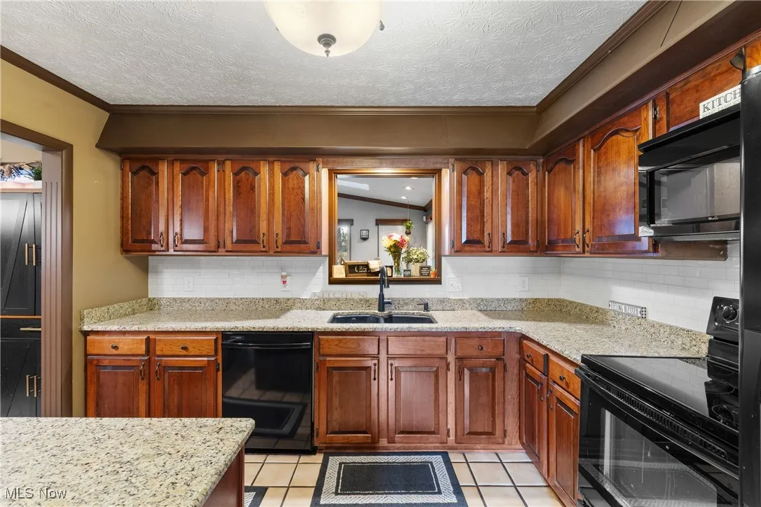 Kitchen featuring black appliances, light stone counters, decorative backsplash, light tile patterned floors, and a textured ceiling