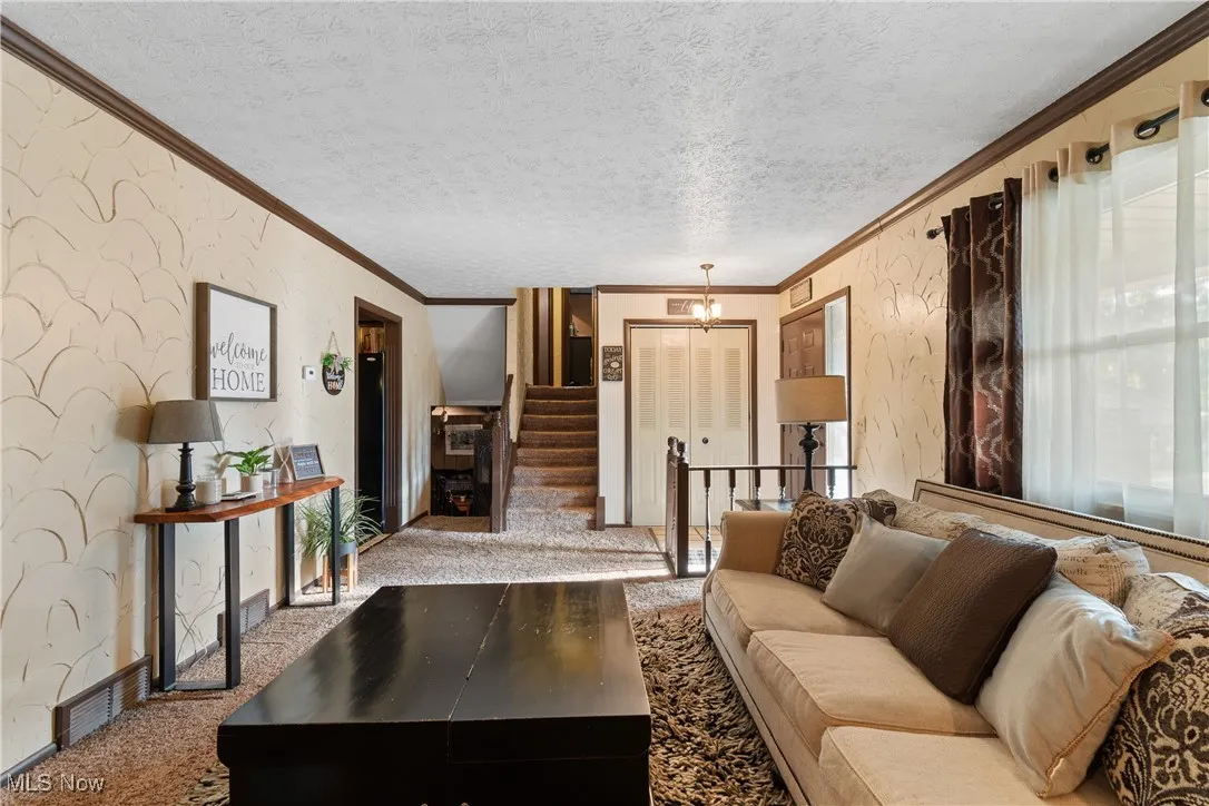 Living room featuring wallpapered walls, crown molding, carpet flooring, a textured ceiling, and a chandelier