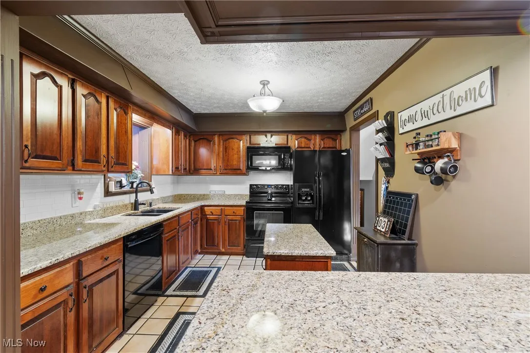 Kitchen featuring black appliances, a textured ceiling, light stone counters, light tile patterned flooring, and ornamental molding