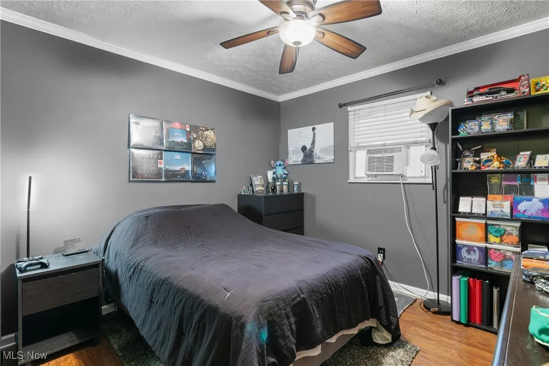 Bedroom with a textured ceiling, wood finished floors, ornamental molding, ceiling fan, and cooling unit