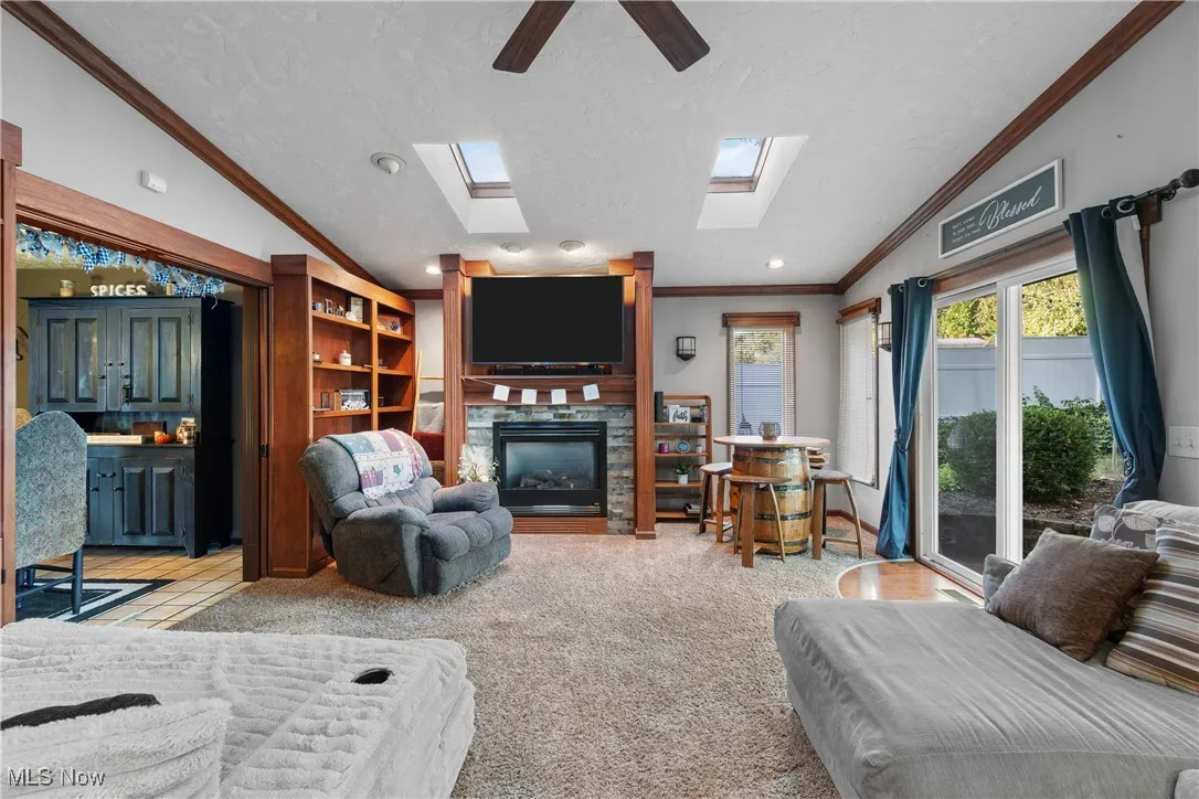 Living room with lofted ceiling, crown molding, a fireplace, ceiling fan, and light colored carpet