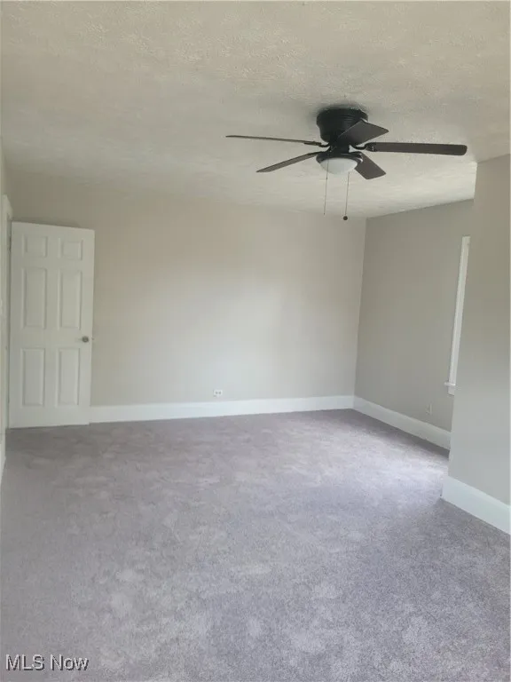 Unfurnished room with a textured ceiling, light colored carpet, and ceiling fan