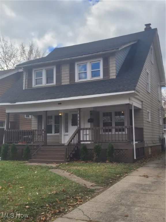 View of front facade with a porch, a front yard, a chimney, and roof with shingles