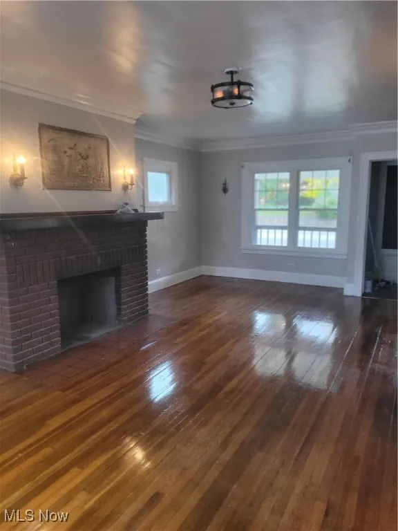 Unfurnished living room featuring a brick fireplace, dark wood-style floors, and ornamental molding