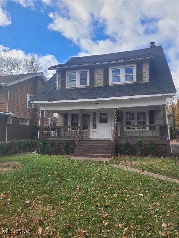 View of front of home with covered porch, a front yard, a shingled roof, and a chimney