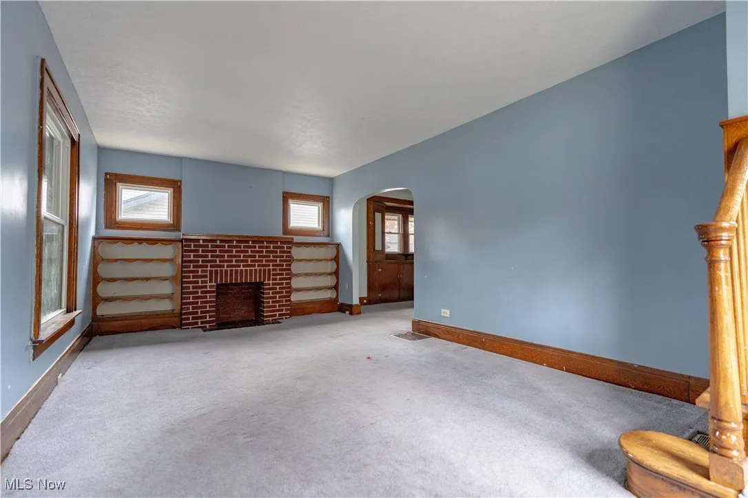 Unfurnished living room with carpet floors, plenty of natural light, arched walkways, and a fireplace